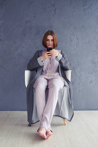 Χαλαρή γυναίκα χρησιμοποιώντας smartphone και να κάθεται στην πολυθρόνα - Φωτογραφία, εικόνα