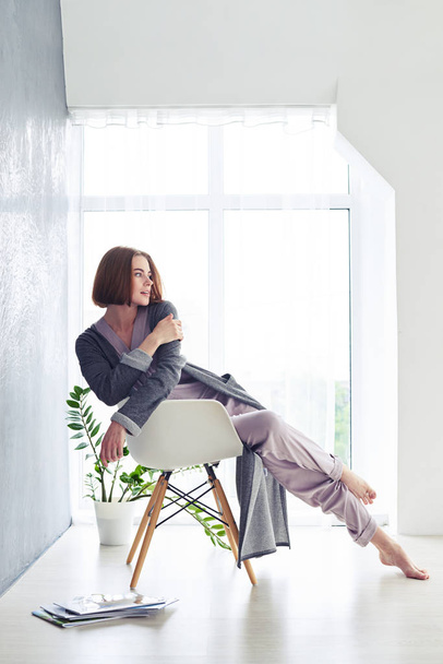 Prachtige vrouw in pyjama genieten van de rust op fauteuil - Foto, afbeelding