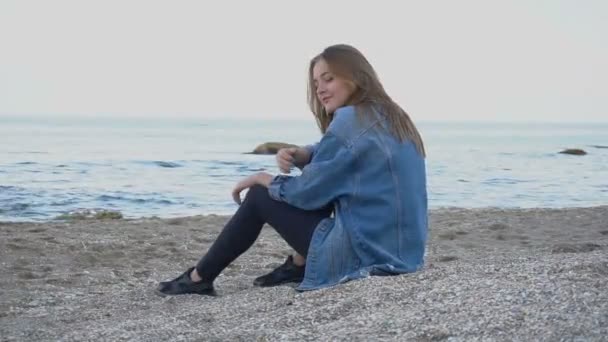 Hermosa joven mujer se relaja sentada en la playa y disfruta de la vista del mar y el cielo en la cálida noche de verano
. - Metraje, vídeo