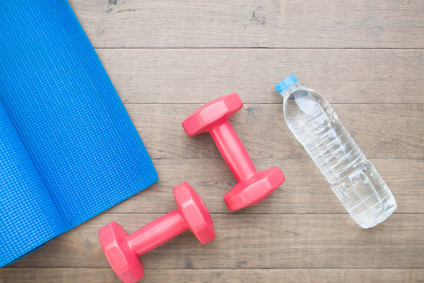 Fitness mat, dumbbells and water on wooden floor - Photo, Image