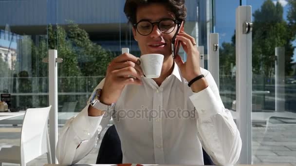 Young man drinking coffee and talking on phone - Кадры, видео