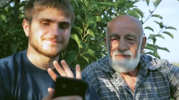 Δύο αγρότες διεξάγουμε μια τηλεδιάσκεψη με ένα smartphone που κάθεται σε ένα οπωρώνα - Πλάνα, βίντεο
