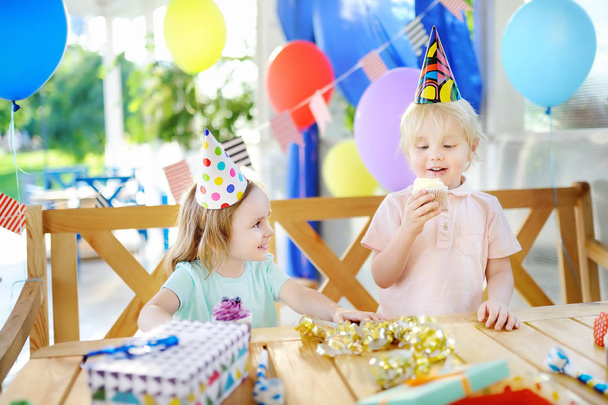 Kleine jongen en meisje hebben plezier en vieren verjaardagsfeest met kleurrijke decoratie en gebak - Foto, afbeelding