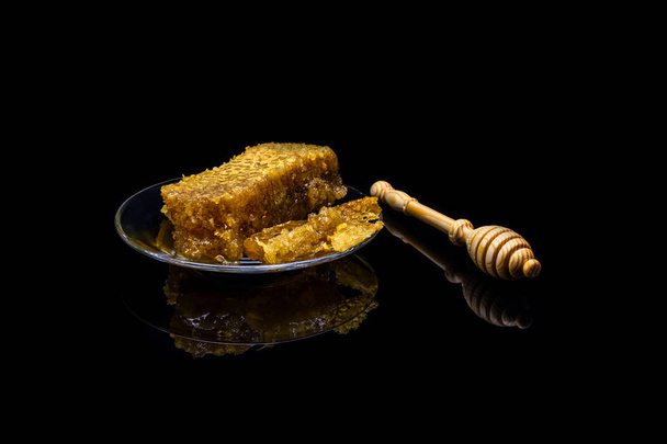 Honey with honeycombs on a glass plate isolated on a black background - Foto, afbeelding