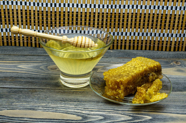 Honey with honeycomb in a glass plate on old wooden table - Фото, зображення