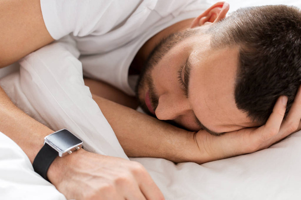 close up of man with smartwatch sleeping in bed - Foto, Imagem