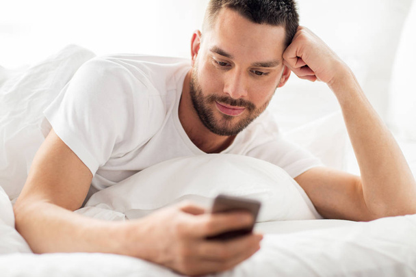 close up of man with smartphone in bed in morning - Zdjęcie, obraz