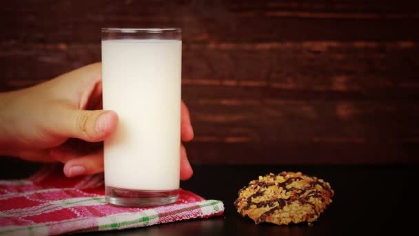 Young man drinking milk and cookie on a wooden background - Πλάνα, βίντεο