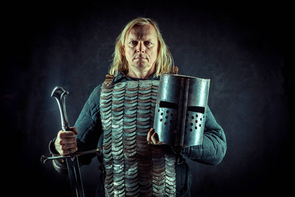 Мощный рыцарь-блондин с мечом и шлемом на темном фоне
. - Фото, изображение