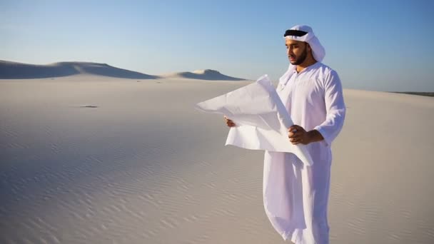 Bölcs muszlim Arab Uae Sheikh építési srác ellenőrzi a területen, és beolvassa a blueprint-építés, a sivatag közepén állva a meleg nap. - Felvétel, videó