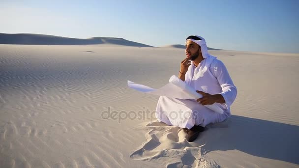Enterprising male sheikh businessman sitting with white paper in hands and thinking of ideas for new project in desert on hot day. - Footage, Video
