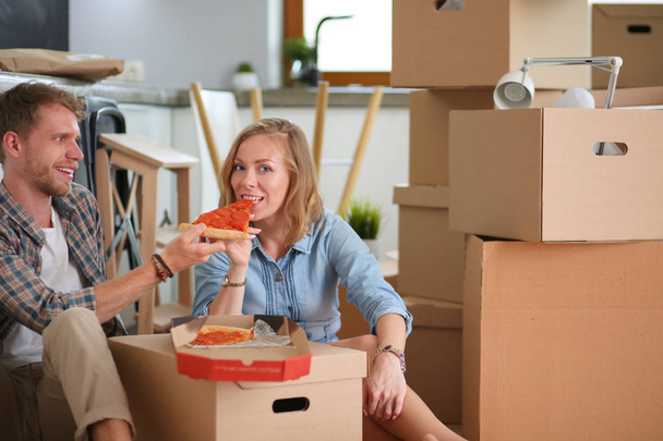 Young couple have a pizza lunch break on the floor after moving into a new home with boxes around them. Young couple - Foto, imagen