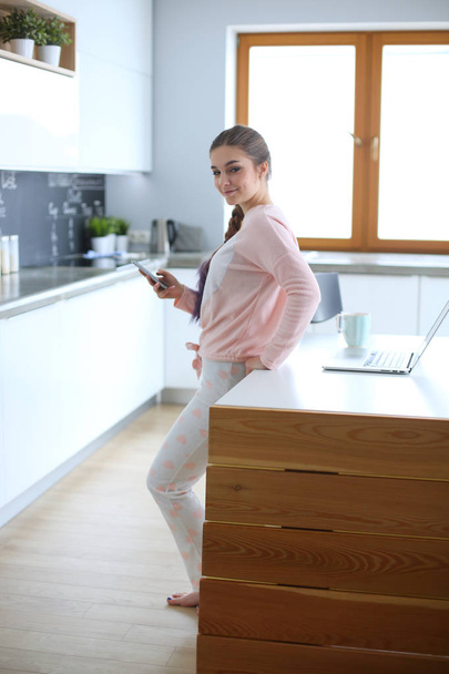 Nainen käyttää matkapuhelinta seisoo modernissa keittiössä
. - Valokuva, kuva