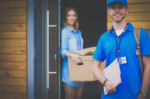 Mavi üniformalı gülümseyen kurye servis konseptine paket kutusu teslim eden teslimatçı. Mavi üniformalı gülümseyen teslimatçı. - Fotoğraf, Görsel