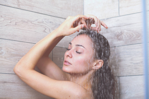 Young beautyful woman under shower in bathroom. - Photo, image