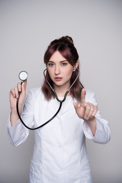 Молодая женщина-врач держит стетоскоп
 - Фото, изображение