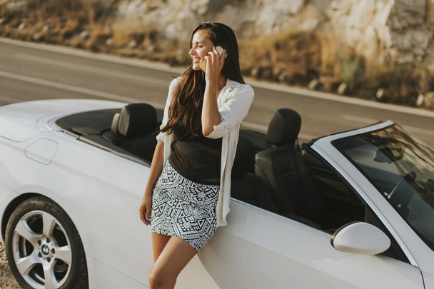 Woman uses a mobile phone and stands next to cabriolet - Photo, Image