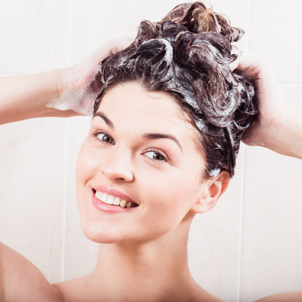 Молода жінка миє волосся шампунем у душі
 - Фото, зображення