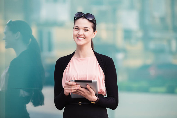 Business woman posing with a tablet and smiling at outdoor near  - 写真・画像