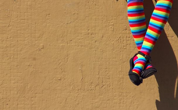 Γυναικεία πόδια σε πολύχρωμες κάλτσες στο φόντο γκρι τείχους. - Φωτογραφία, εικόνα