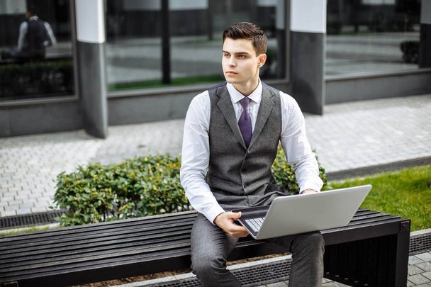 Handsome young businessman working on laptop outdoors on a background of corporate building.  - Valokuva, kuva