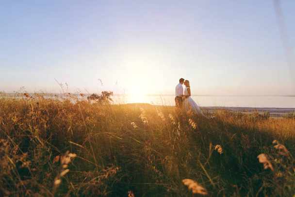 Bride and groom are walking together at sunset near the sea - Photo, image