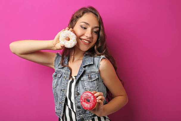 Portrait of young woman with sweet donuts on pink background - 写真・画像