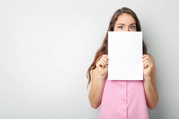 Young woman with blank paper on grey background - Foto, Bild
