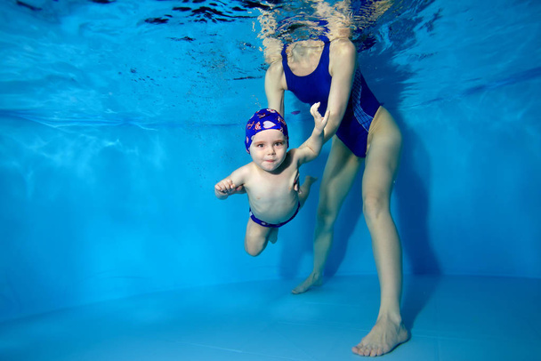 Máma pomáhá syna plavat pod vodou v bazénu na modrém pozadí. - Fotografie, Obrázek