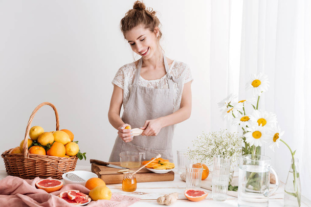 Lady standing indoors and squeezes out juice of a citruses - Photo, image