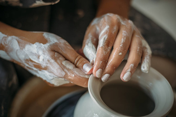 Dirty hands in white clay, pottery wheel with bowl or jar. Potter at work, woman's hands - Fotografie, Obrázek