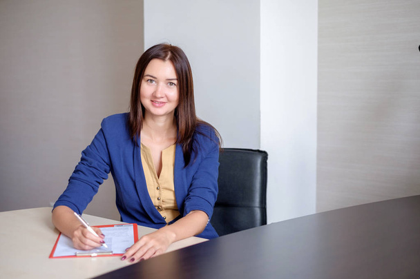 Young businesswoman working at desk in office, taking notes into personal calendar, smiling. - Фото, зображення