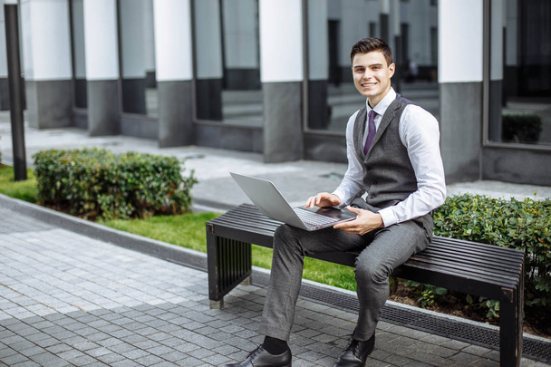 Portrait of a successful young man working on laptop on bench outdoors - Foto, Bild
