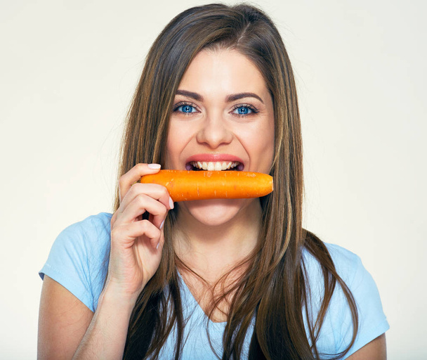 Smiling woman bites carrot. Isolated studio portrait. - Фото, изображение