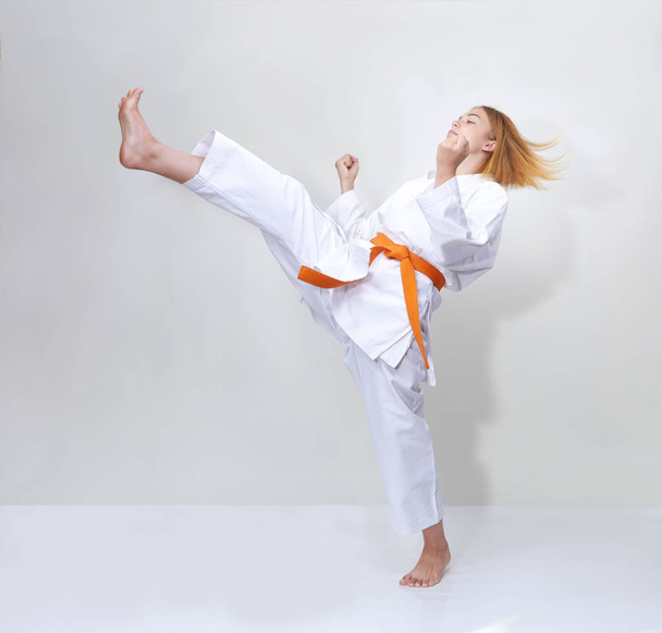 Sportswoman with an orange belt beats a kick on a gray background - Photo, Image