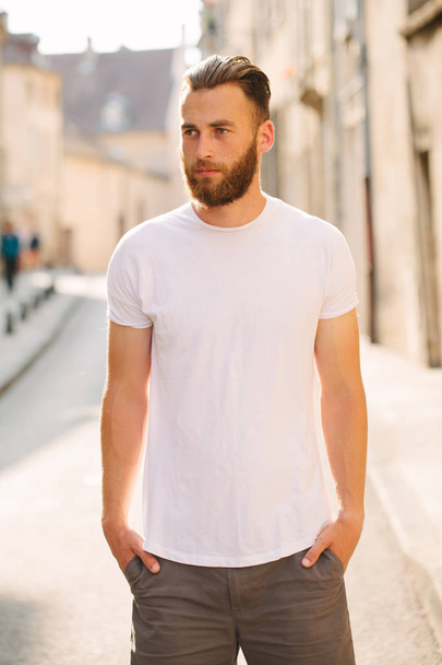 Hipster handsome male model with beard wearing white blank t-shirt with space for your logo or design in casual urban style - Фото, зображення
