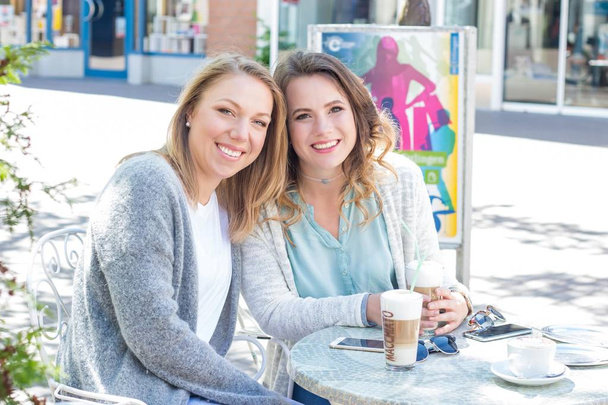 Deux amis traversent la ville et boivent du cappuccino. Deux jeunes femmes assises au Café. Communication Ressort chaud. Été
. - Photo, image
