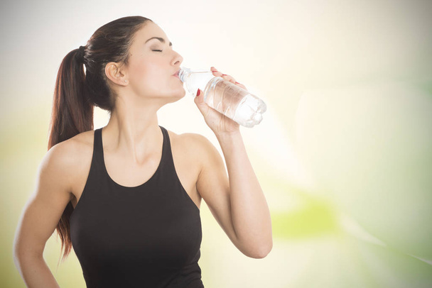 Здорова і спортивна молода жінка п'є воду з пляшки
 - Фото, зображення
