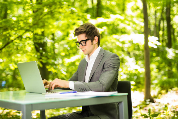 Side portrait of young handsome business man working at laptop at office table in green park. Business concept. - Photo, Image