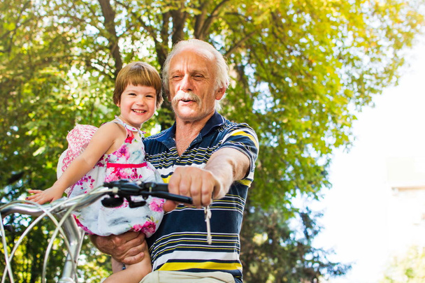 Büyükbaba binicilik bisiklet ile torunu elinde - Fotoğraf, Görsel