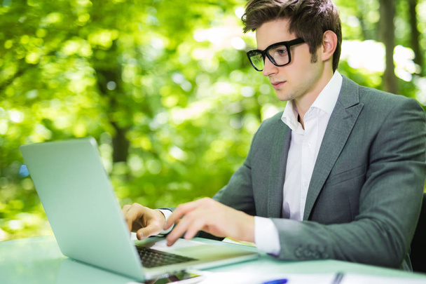 Молодий красивий менеджер працює за ноутбуком за офісним столом у зеленому парку. Концепція бізнесу
. - Фото, зображення