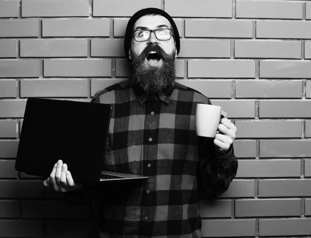 Bearded brutal caucasian hipster holding laptop with cup - Photo, image