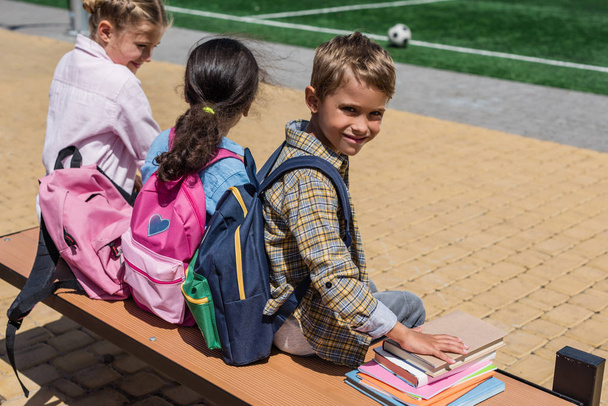 schoolkids s knihami sedí na lavičce - Fotografie, Obrázek