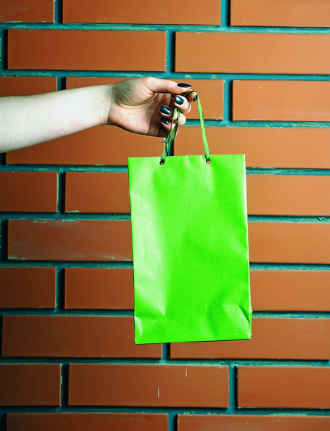 green shopping bag in female hand on brick wall - Photo, image
