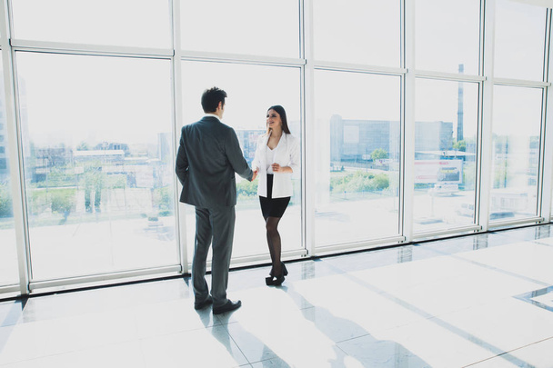 Two young businessman and business woman are standing in modern office with panoramic windows. - 写真・画像