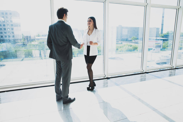 Two young businessman and business woman are standing in modern office with panoramic windows. - Photo, image