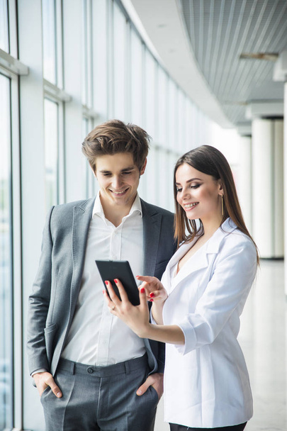 Cheerful business woman and man working together on tablet in office hall - Photo, Image