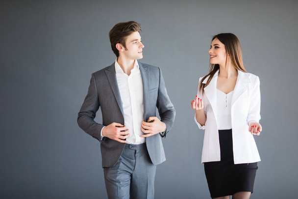 Smiling businesswoman and businessman are conversing against grey background. Business concept. - Fotografie, Obrázek