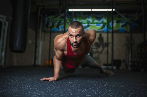 A handsome man with a muscular body on a blurred background. Sexy muscle man is doing a push-up in the gym. Sports activity. - Foto, afbeelding