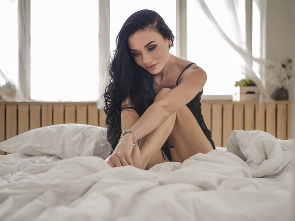 Primo piano di giovane donna sexy in lingerie in posa sul letto con bellissimi occhi grigi. Bruna ragazza con biancheria intima nera nella sua camera da letto
 - Foto, immagini